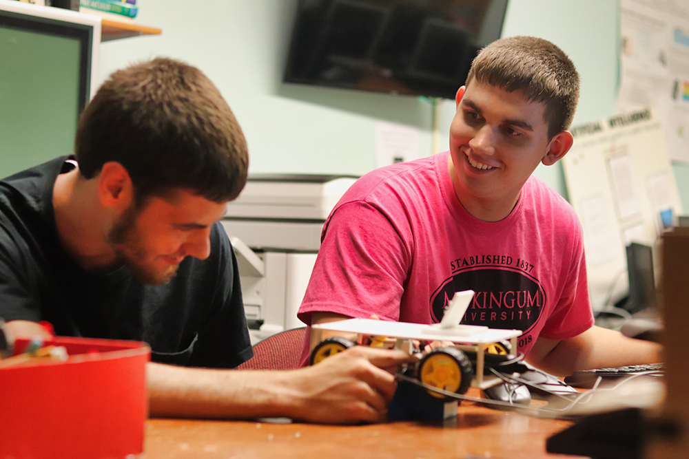 2 male students building a 3d printed remote control car that uses AI technology to drive