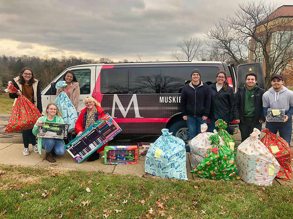 group shot of the students involve holding the gifts that they are donating.  Standing in front of the MU van, getting ready to load it full of toys.