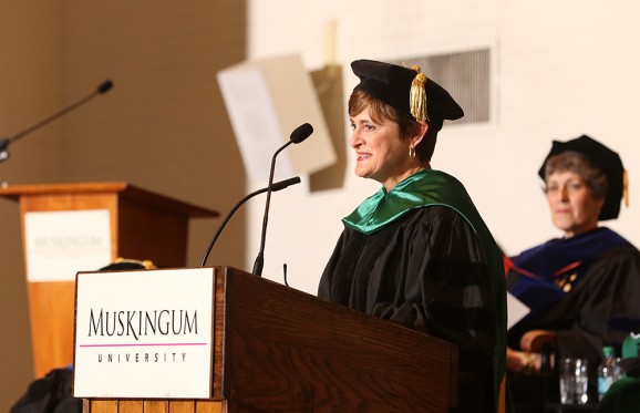 Kim Rothermel speaking a at podium in regalia attire