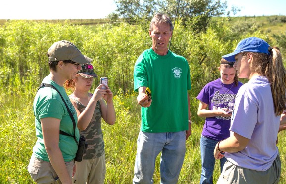 Students with Professor Ingold at the Wilds inspecting a yellow bird that he is holding in his hand