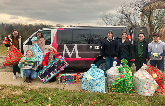 group shot of the students involve holding the gifts that they are donating.  Standing in front of the MU van, getting ready to load it full of toys.