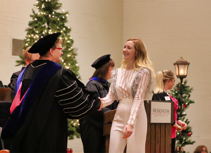 a blonde female student dressed in white crossing the stage and shaking hands with President Hasseler