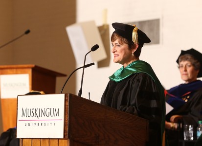 Kim Rothermel speaking a at podium in regalia attire