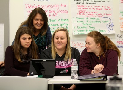 3 female education students in a group with teacher leaning over table disccussing their project