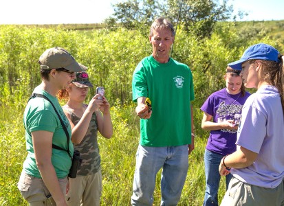 Students with Professor Ingold at the Wilds inspecting a yellow bird that he is holding in his hand