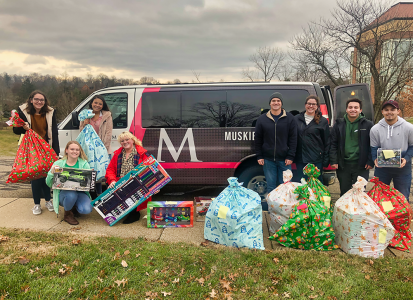 group shot of the students involve holding the gifts that they are donating.  Standing in front of the MU van, getting ready to load it full of toys.